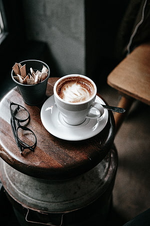 Rustic Coffee Cup With Latte Art, Sugar Packets, And Glasses On A Wooden Side Table HD phone wallpaper
