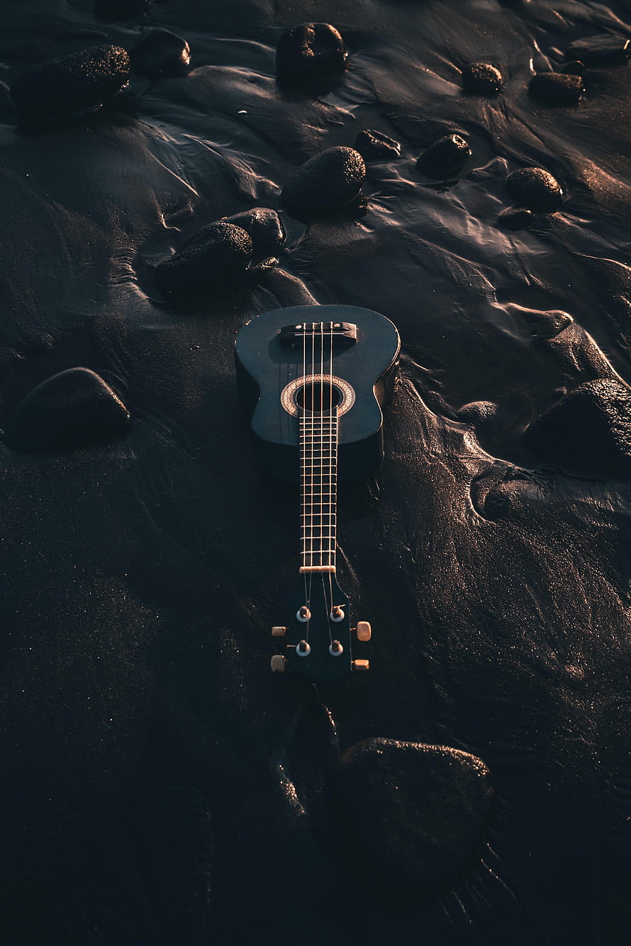 Black Ukulele Resting on Wet Sand and Rocks at a Dark Beach HD phone wallpaper