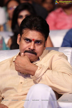 Pawan Kalyan in a cream shirt with a red tilak, seated at a public event with a serious expression HD phone wallpaper