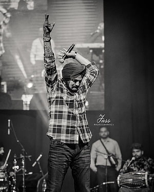 Diljit Dosanjh performing live on stage in a plaid shirt and turban, black and white concert photography HD phone wallpaper
