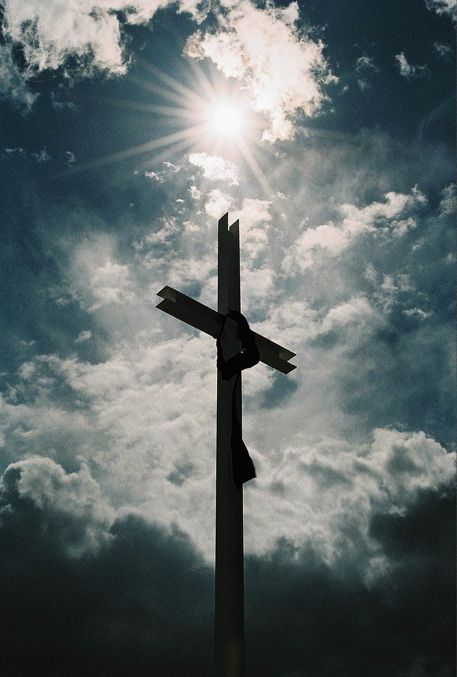 Silhouette of a wooden cross against a dramatic cloudy sky with bright sun rays shining through HD phone wallpaper