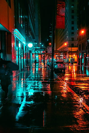 Neon-lit rainy city street at night with wet pavement reflections and pedestrians under umbrellas HD phone wallpaper