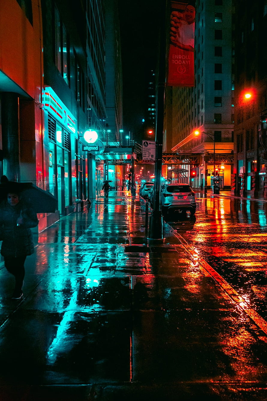Neon-lit rainy city street at night with wet pavement reflections and pedestrians under umbrellas HD phone wallpaper