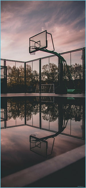 Empty outdoor basketball court at dusk with a perfect reflection in a puddle under a pink and purple sky HD phone wallpaper