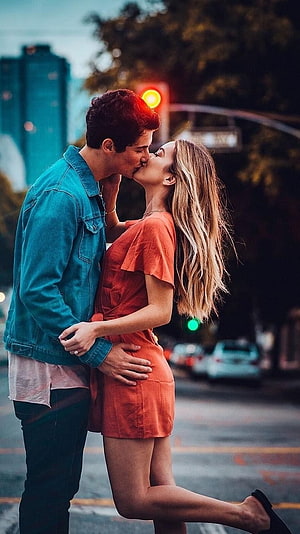 Romantic couple sharing a kiss on a city street at dusk with warm ambient lighting HD phone wallpaper