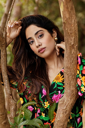 Janhvi Kapoor in a vibrant floral dress posing among tree branches in a natural outdoor setting HD phone wallpaper