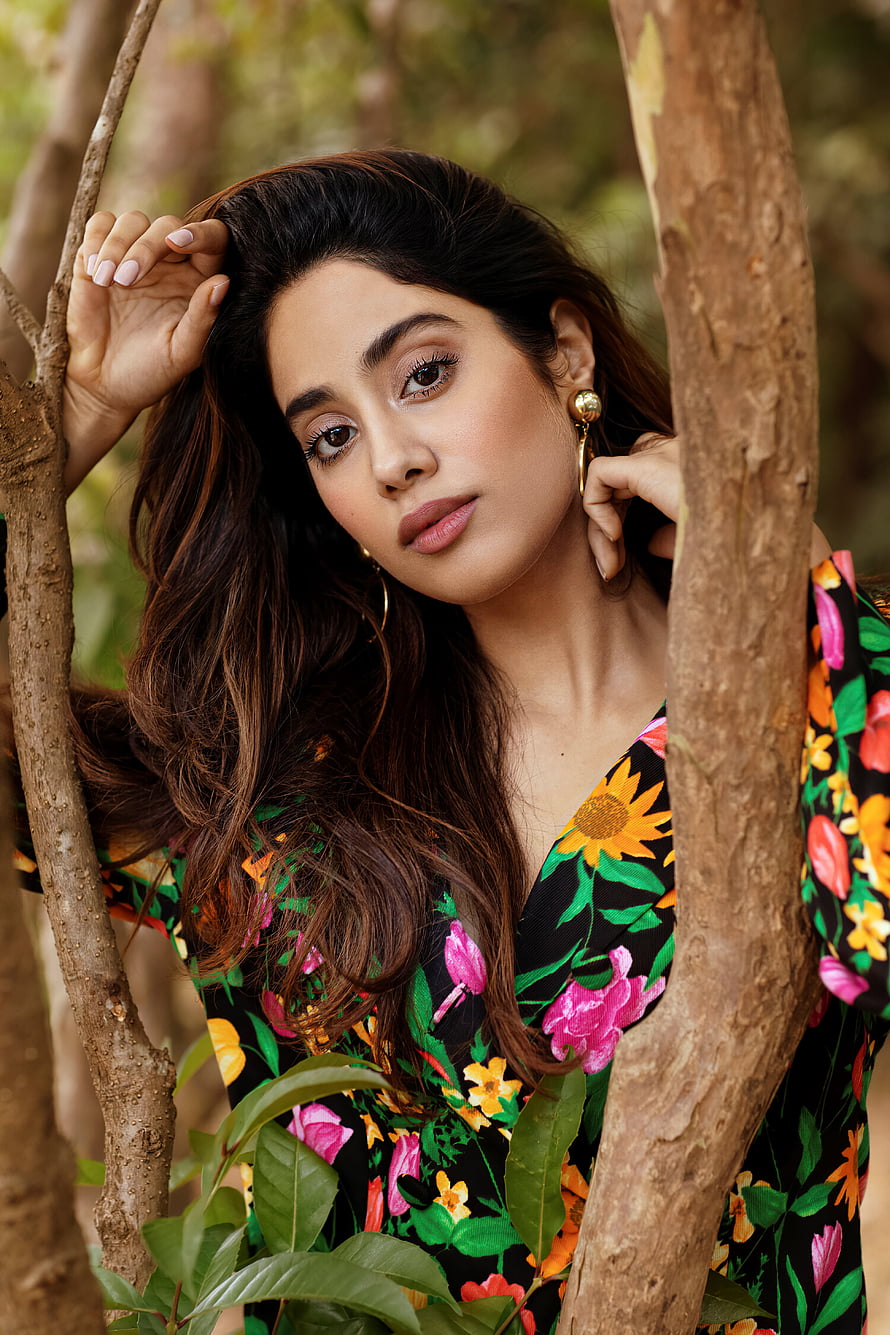 Janhvi Kapoor in a vibrant floral dress posing among tree branches in a natural outdoor setting HD phone wallpaper