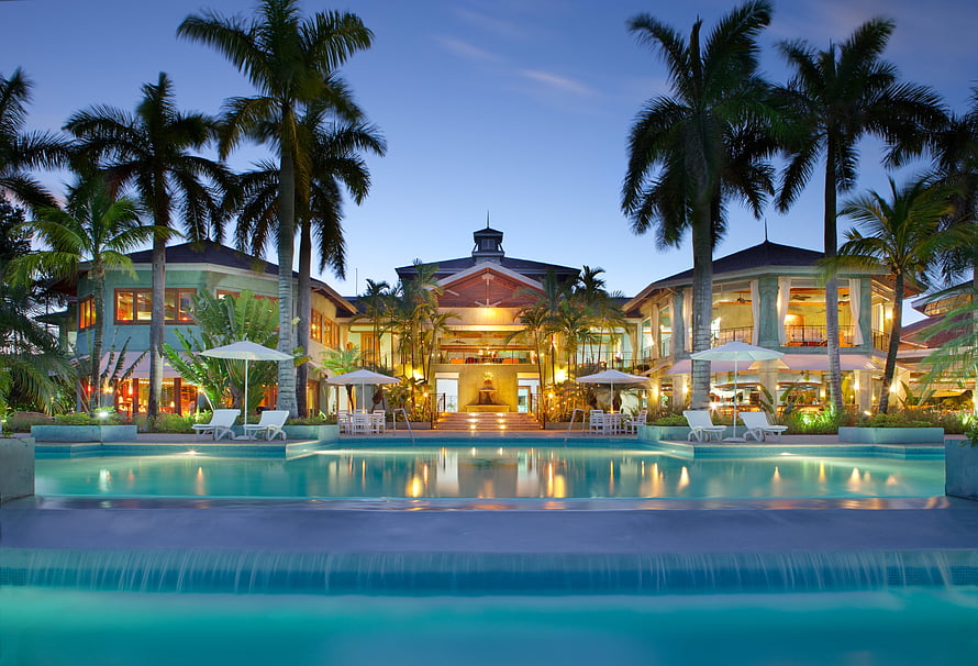 Luxury tropical resort with illuminated swimming pool and palm trees at dusk HD wallpaper