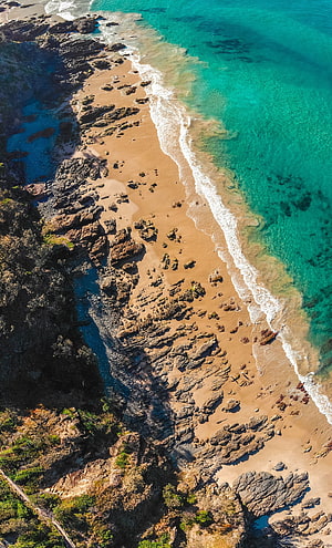 Aerial View of Rocky Coastline with Turquoise Ocean and Sandy Beach HD phone wallpaper
