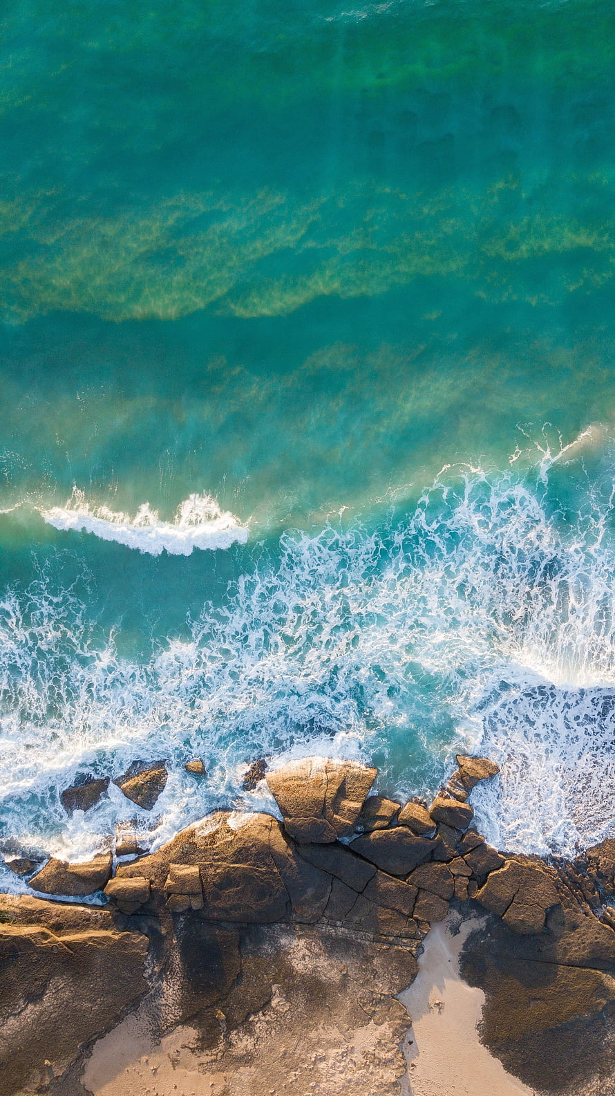 Aerial View of Turquoise Ocean Waves Crashing Against Rocky Coastline HD phone wallpaper