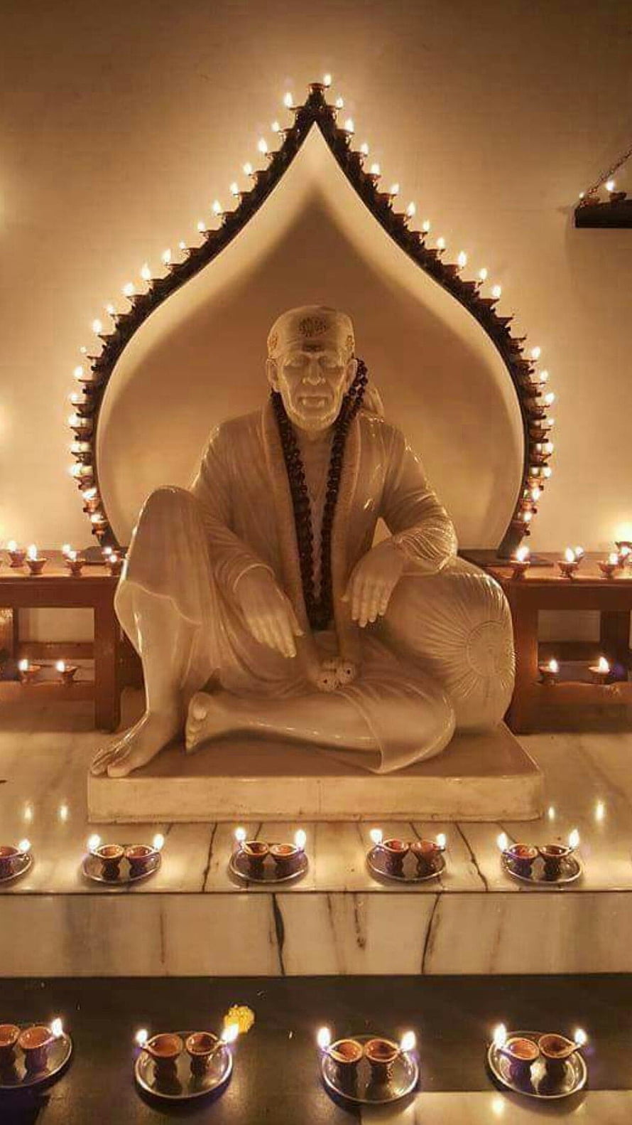 Serene Statue of Sai Baba Surrounded by Glowing Oil Lamps and Decorative Arch HD phone wallpaper