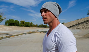Johnny Sins in a grey beanie and white t-shirt standing in a concrete canal under a blue sky HD wallpaper