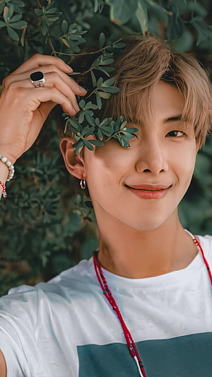 RM of BTS smiling with green leaves near his eye in a white t-shirt HD phone wallpaper