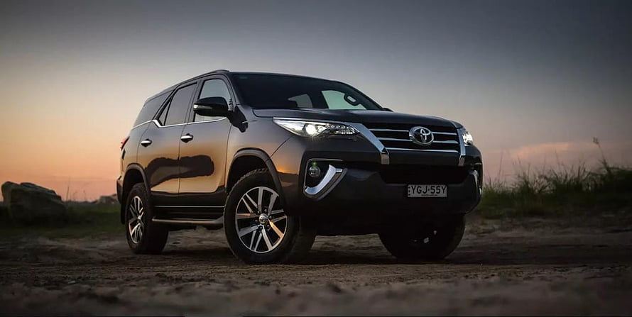Black Toyota Fortuner SUV parked on a dirt road at sunset with dramatic sky and warm lighting HD wallpaper