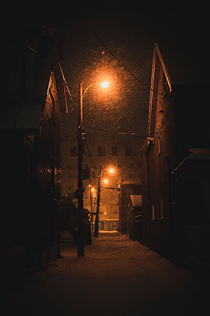 Snowy Urban Alleyway at Night Illuminated by Warm Street Lamps HD phone wallpaper