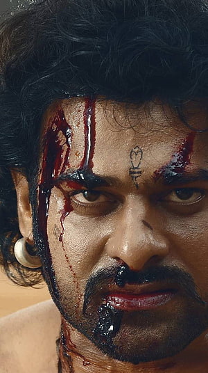 Prabhas as Baahubali in a blood-soaked close-up with intense gaze and forehead symbol HD phone wallpaper