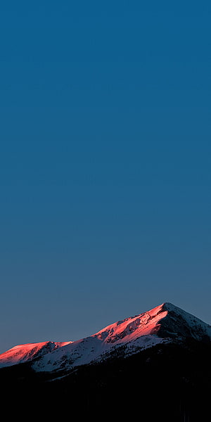 Snow-Capped Mountain Peak Bathed in Warm Sunset Glow Against Deep Blue Sky HD phone wallpaper