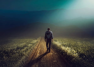Lone Explorer Walking a Dirt Path Through a Misty Mountain Valley at Dawn HD wallpaper