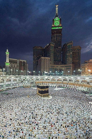 Night view of the Kaaba in Mecca with the Abraj Al Bait clock tower and massive crowd of pilgrims praying HD phone wallpaper