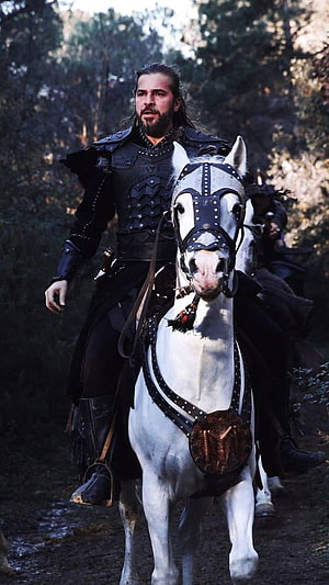 Ertugrul Gazi in Black Armor Riding a White Horse Through a Forest HD phone wallpaper