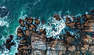 Aerial View of Turquoise Ocean Waves Crashing Against Rugged Rocky Coastline HD wallpaper