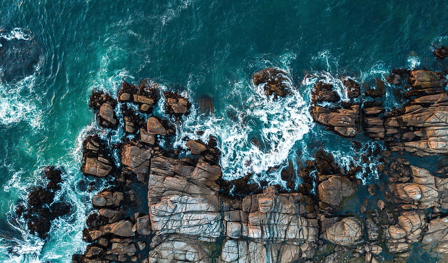 Aerial View of Turquoise Ocean Waves Crashing Against Rugged Rocky Coastline HD wallpaper
