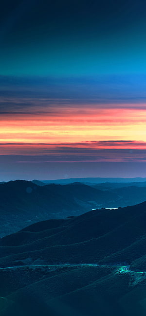 Vibrant Sunset Over Layered Mountain Ridges with Winding Road and Blue Lens Flare HD phone wallpaper