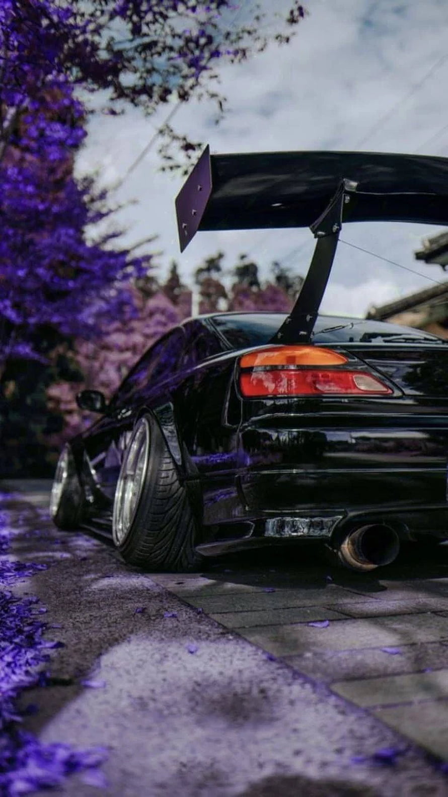 Black JDM Sports Car with Large Rear Wing Parked Under Purple Blossoms HD phone wallpaper