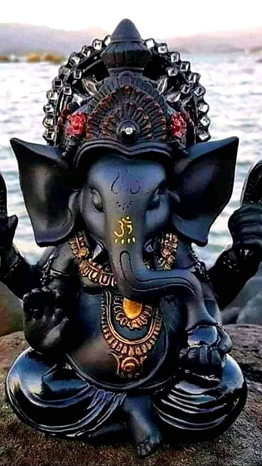 Black Ganesh Statue with Ornate Gold Jewelry and River Background HD phone wallpaper