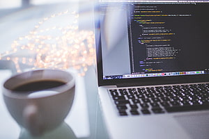Laptop displaying code editor with coffee cup and bokeh lights on desk HD wallpaper