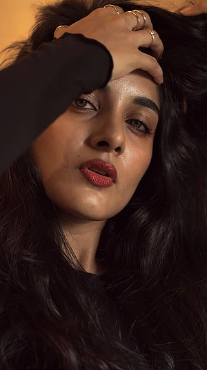 Portrait of Kiara Advani with hand on forehead, dark wavy hair, red lipstick, gold rings, warm lighting, moody close-up HD phone wallpaper