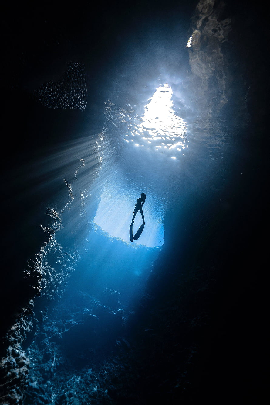 Silhouetted Free Diver Descending Through Sunlit Underwater Cavern HD phone wallpaper