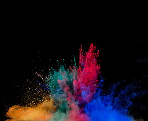 Vibrant multicolored powder explosion bursting against a dark black background HD wallpaper