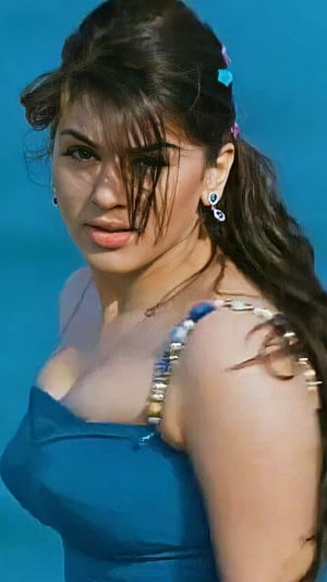 Hansika Motwani in a blue dress with wavy hair and dangling earrings against a blue background HD phone wallpaper