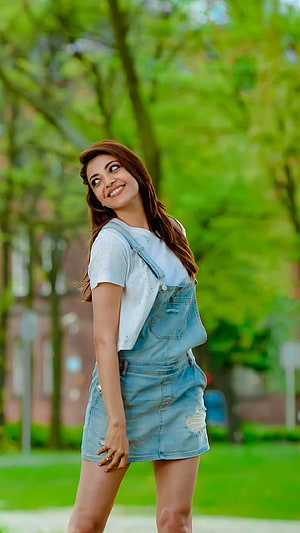 Kajal Agarwal in Denim Overalls and White T-Shirt in a Lush Green Park HD phone wallpaper