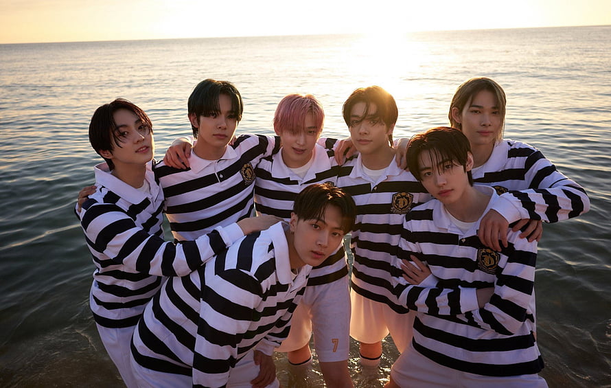 ENHYPEN members posing in matching black and white striped rugby shirts at the ocean during sunset HD wallpaper