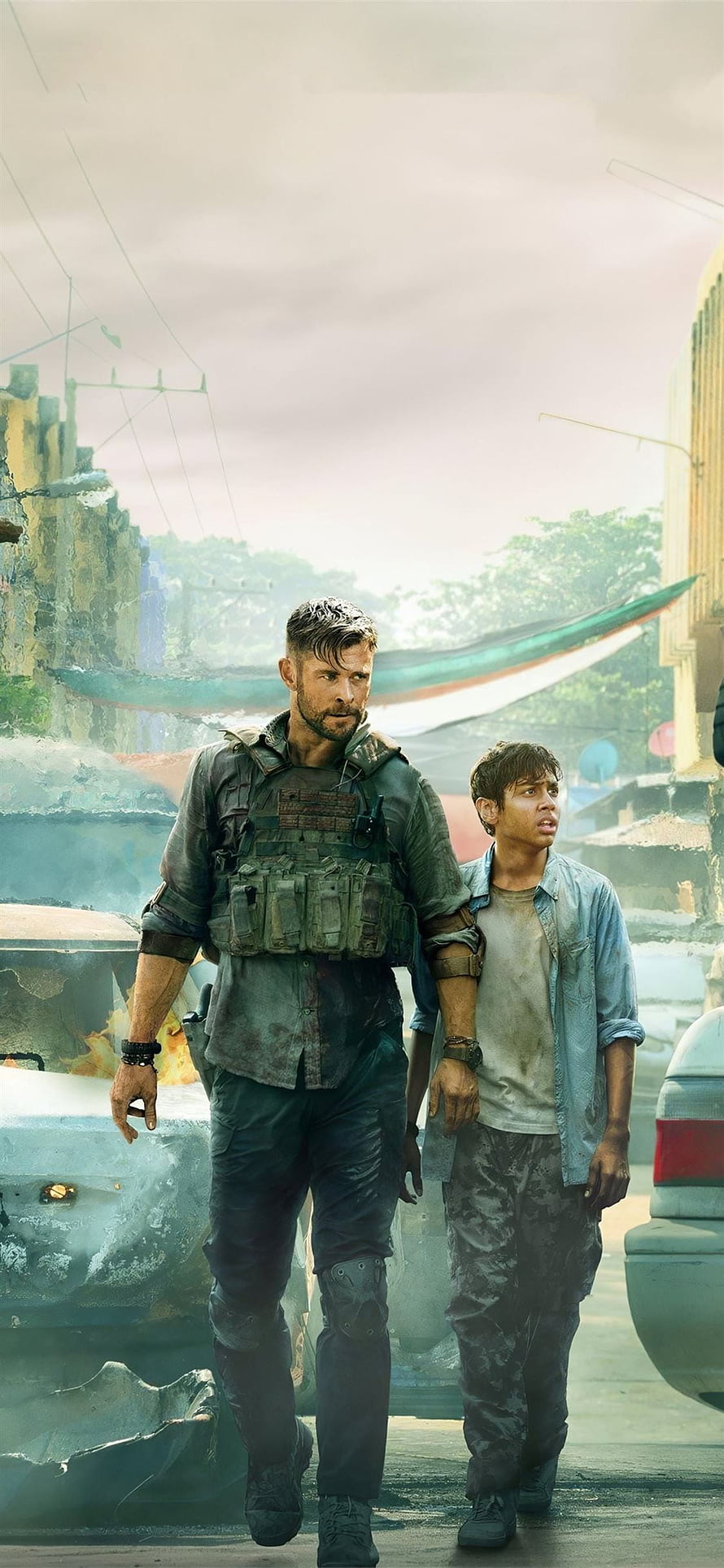 Chris Hemsworth in tactical gear walking through a war-torn urban street with a young boy in the action film Extraction HD phone wallpaper