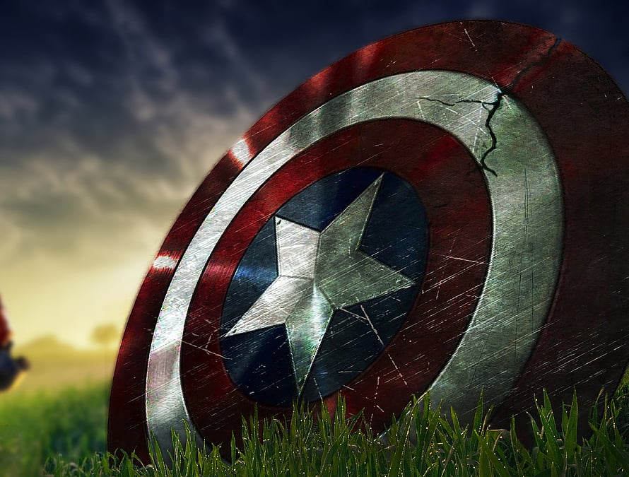 Weathered Captain America Shield Resting in Grass Under Dramatic Sky HD wallpaper
