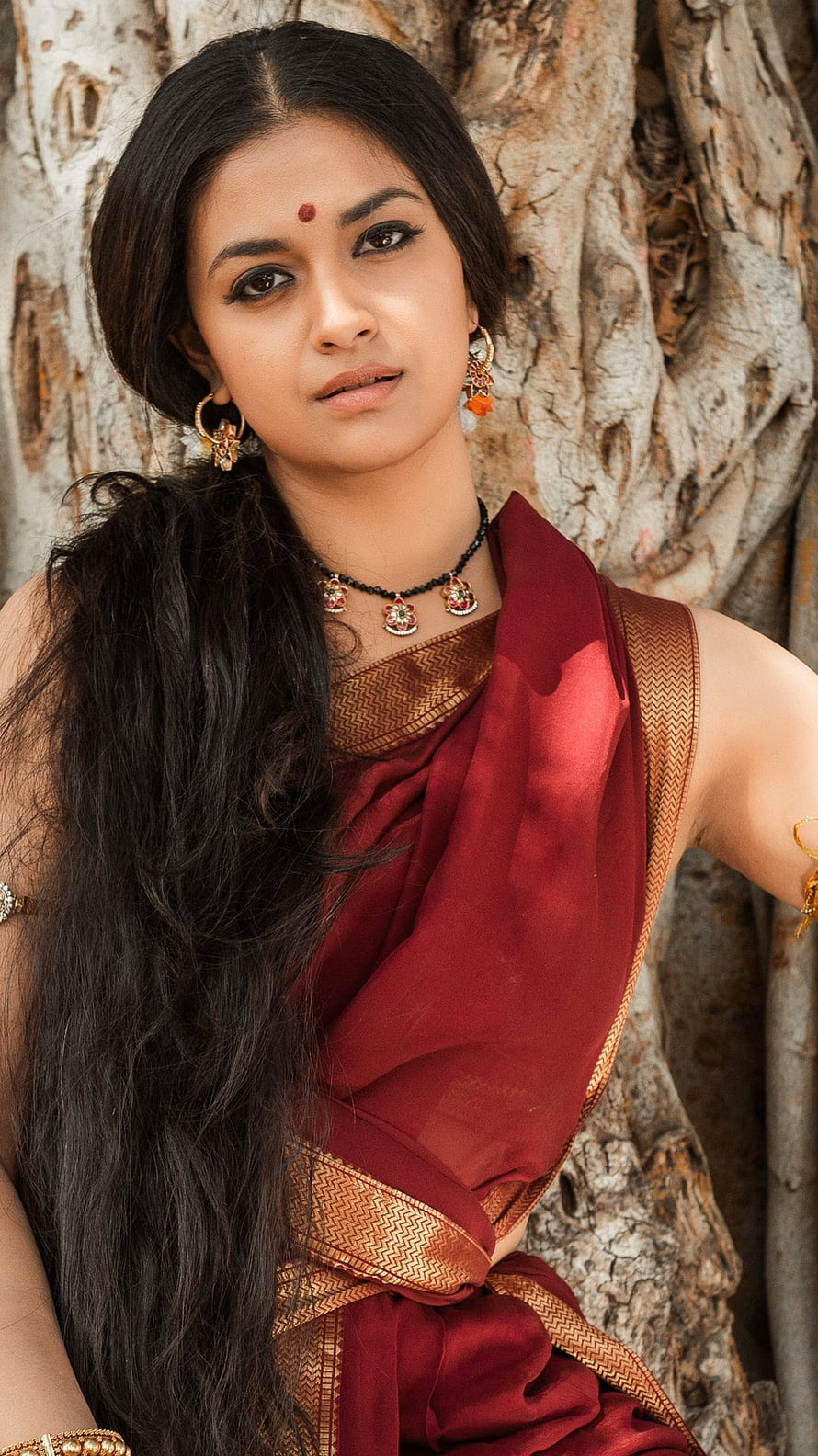Portrait of a woman in a traditional red saree with gold jewelry standing by a tree, Keerthi Suresh, actress, keerthysuresh, keerthy, bollywood, keerthy suresh, Tollywood, keerthisuresh HD phone wallpaper