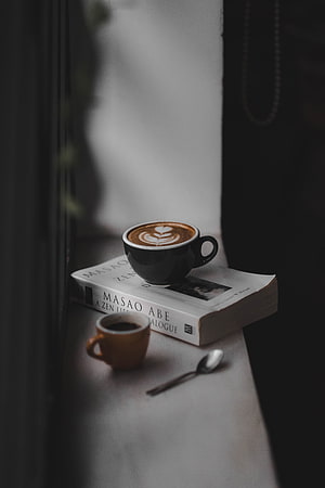 Cozy Latte Art Coffee Cup Resting on a Book by a Window Sill HD phone wallpaper
