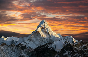 Majestic Snow-Capped Mountain Peak Under a Dramatic Orange Sunset Sky HD wallpaper