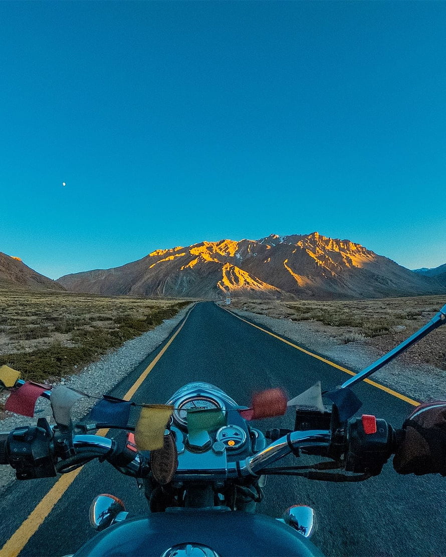 First-person motorcycle ride on a desert highway toward golden-lit Himalayan peaks at dusk HD phone wallpaper