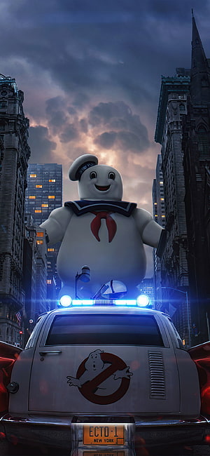 Cute Ghostbusters Mascot Standing on Ecto-1 in a Dramatic City Street at Dusk HD phone wallpaper