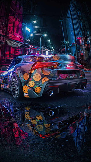Toyota GR Supra with smiley face wrap parked on wet neon street at night HD phone wallpaper