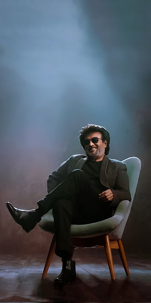 Rajinikanth sitting in a chair wearing sunglasses and a dark suit with dramatic lighting HD phone wallpaper