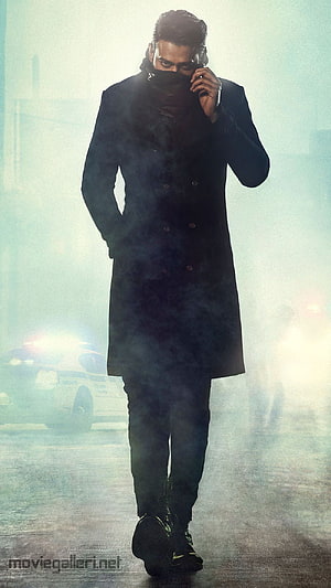 Prabhas as Saaho in a dark trench coat walking through smoke with a police car in the background HD phone wallpaper