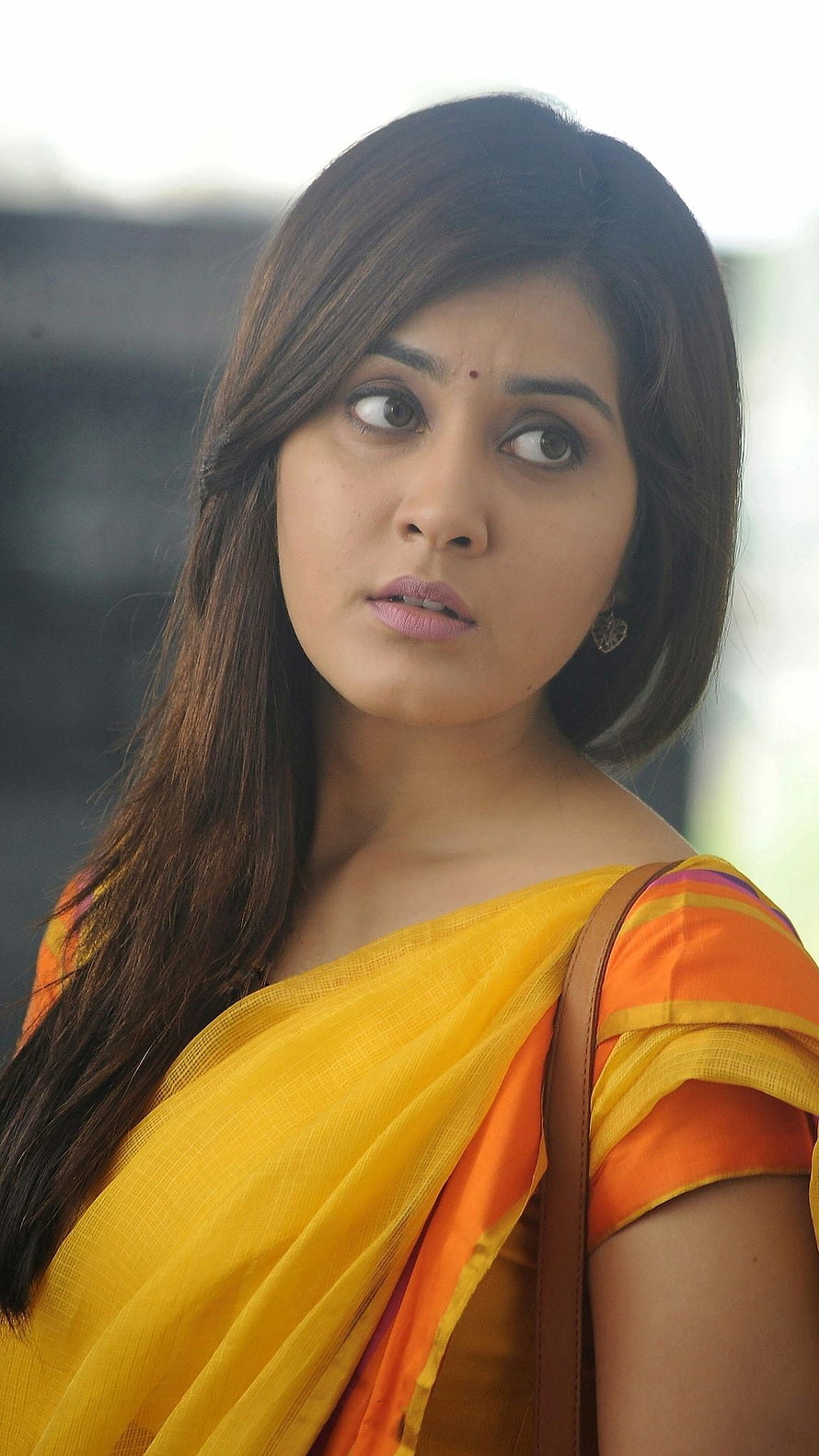 Rashi Khanna in a vibrant yellow and orange saree with a contemplative expression HD phone wallpaper