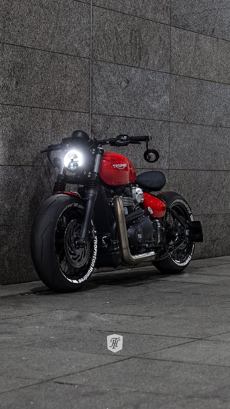 Red Triumph Bobber Motorcycle Parked Against Grey Stone Wall HD phone wallpaper