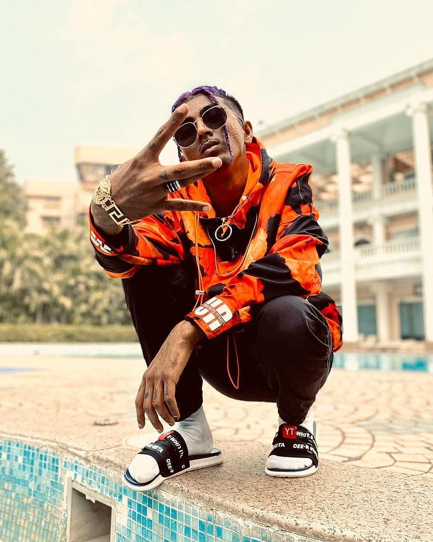 MC Stan posing in vibrant orange streetwear by a resort pool HD phone wallpaper
