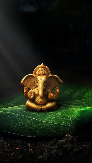 Golden Ganesha Idol Sitting on Green Leaf with Dramatic Lighting HD phone wallpaper